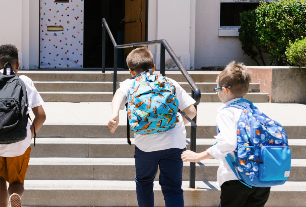 Three school children wearing backpacks run up steps