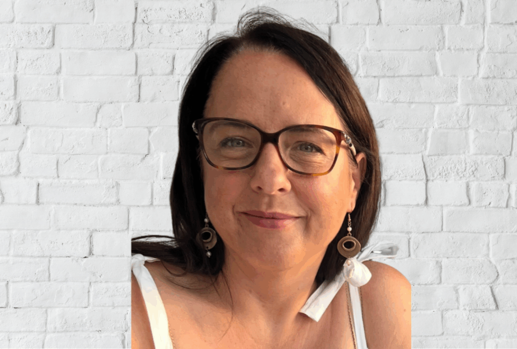 Jayne Bogle Jayne is positioned in front of a white brick wall, shown from the shoulders up. Jayne has shoulder‑length dark hair and is wearing a sleeveless white top with tied straps.