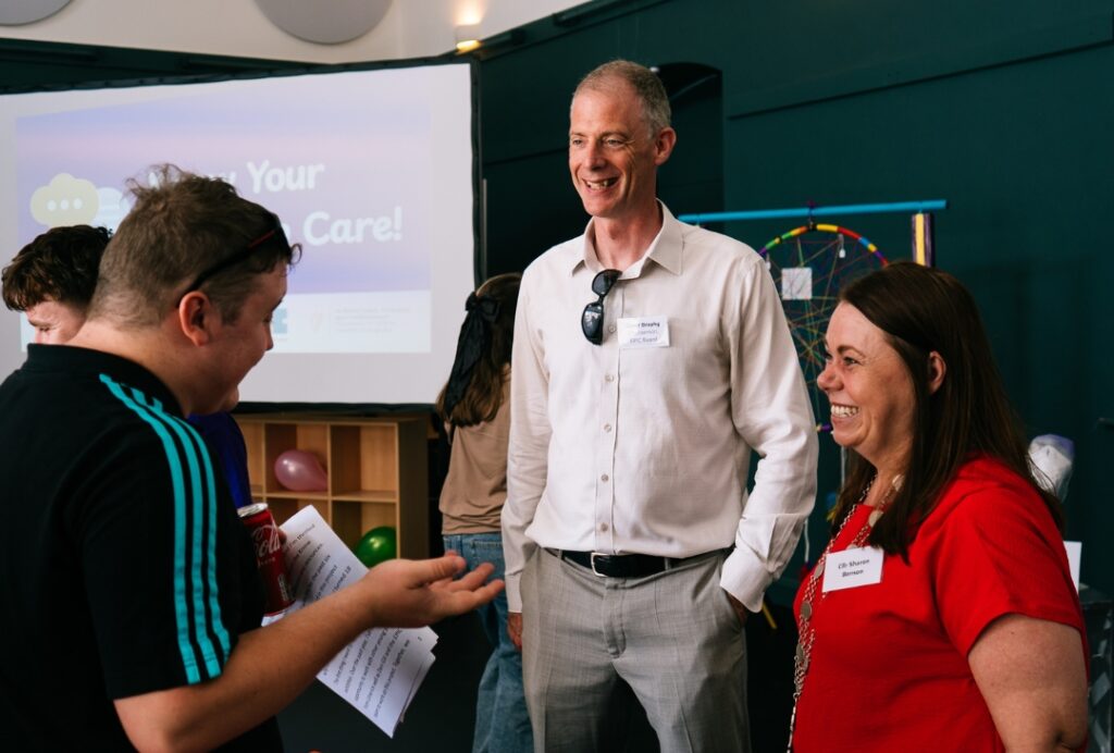 One artist in the foreground holds a document while speaking with two attendees wearing name badges.